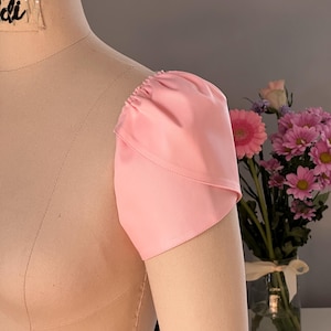 Op de afbeelding: Een close-up van een roze stoffen mouw met een geplooide ruche aan de bovenkant. De mouw zit op een paspop.