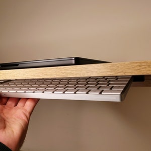 Könnte beinhalten: Eine weiße Tastatur ist unter einem Holztisch montiert, mit einem schwarzen Laptop auf dem Tisch. Die Tastatur ist herausgezogen und einsatzbereit.