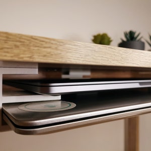 Könnte beinhalten: Ein weißer Laptop-Ständer, der an der Unterseite eines Holzschreibtisches befestigt ist. Der Ständer hält zwei Laptops, einen übereinander.