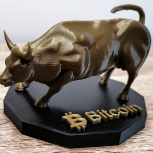 Può includere: Una statua di toro dorata stampata in 3D su una base nera con la scritta "Bitcoin" stampata su di essa.
