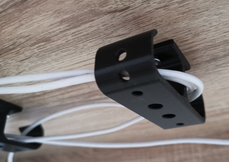 Puede incluir: Clip de gesti&oacute;n de cables de pl&aacute;stico negro con m&uacute;ltiples agujeros para organizar los cables. Los cables blancos se enhebran a trav&eacute;s del clip.