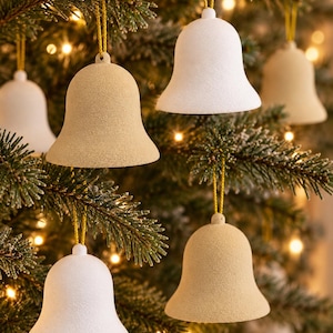 Pode incluir: Uma coleção de ornamentos em forma de sino pendurados em ramos. Os ornamentos apresentam um acabamento mate e texturado em tons alternados de branco sujo e bege claro. Cada sino está suspenso por um fio fino de cor dourada.