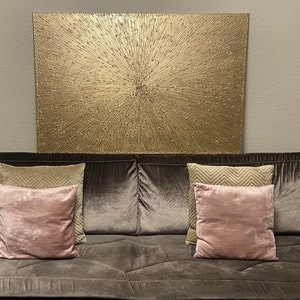May include: A brown velvet sofa with two beige and two pink throw pillows. A large gold abstract painting hangs above the sofa.