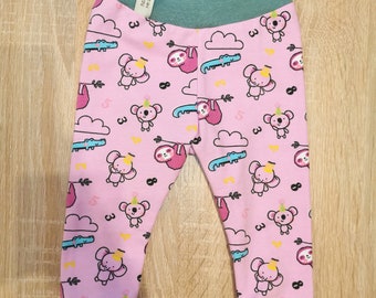 Op de afbeelding: Roze baby leggings met een groene tailleband en boorden. De leggings hebben een herhalend patroon van koala's, luiaards, alligators en wolken. De tekst "3" verschijnt in het hele patroon.