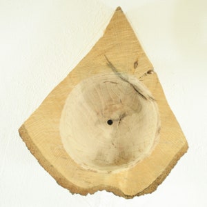 May include: A wooden bowl carved from a tree trunk with a natural, irregular edge. The bowl has a smooth, rounded interior and a small hole in the center.