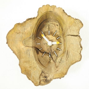 May include: A wooden clock with a natural wood finish and a white face with black markings. The clock is set into a circular piece of wood with a rough, natural edge.