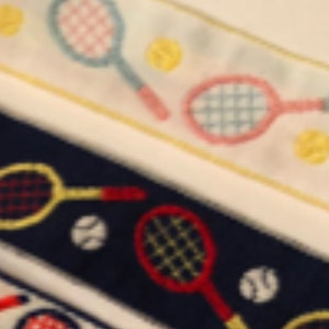 May include: A close-up of three different fabric trims featuring embroidered tennis rackets and tennis balls. The trims are in white, navy blue, and white with yellow accents.