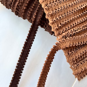 May include: Two brown velvet trims with a ruffled texture. The trim on the left is a darker brown and the trim on the right is a lighter brown.