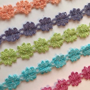 May include: Five different colors of delicate floral lace trim. The trim is made of a soft, woven fabric and features a repeating pattern of small flowers. The colors are peach, purple, green, blue, and pink.