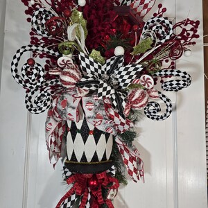 May include: A black and white harlequin jester hat Christmas swag with red and white ribbon, red berries, and candy canes.