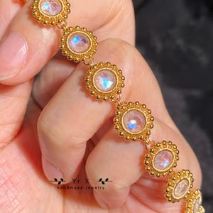 May include: A gold bracelet with iridescent moonstone gemstones set in a circular bezel. The bracelet is made with small gold beads and has a delicate, feminine design.