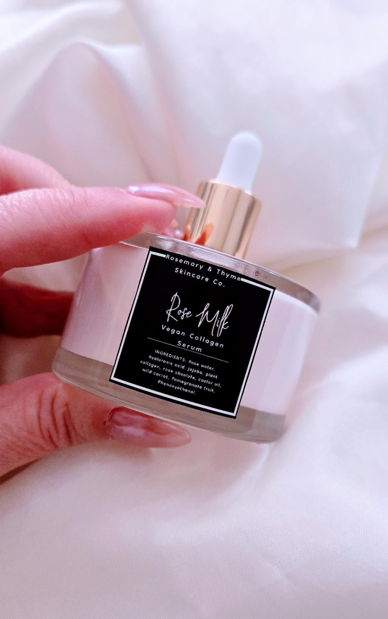 May include: A clear glass bottle of Rose Milk Vegan Collagen Serum with a white dropper and gold-colored top. The bottle has a pink label with black text that lists the ingredients. The product is from Rosemary & Thyme Skincare Co.