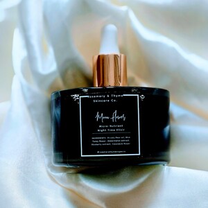 May include: A black glass bottle with a white dropper cap and a square label. The label reads Rosemary & Thyme Skincare Co., Moon Flower, Micro-Nutrient Night Time Elixir, and lists ingredients including Prickly Pear oil, Blue Tansy flower, and Watermelon extract.