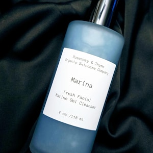 Może przedstawiać: Niebieska szklana butelka "Marina Fresh Facial Marine Gel Cleanser" z Rosemary & Thyme Organic Skincare Company. Butelka ma srebrną pompkę i białą etykietę z informacjami o produkcie. Butelka zawiera 118 ml produktu.