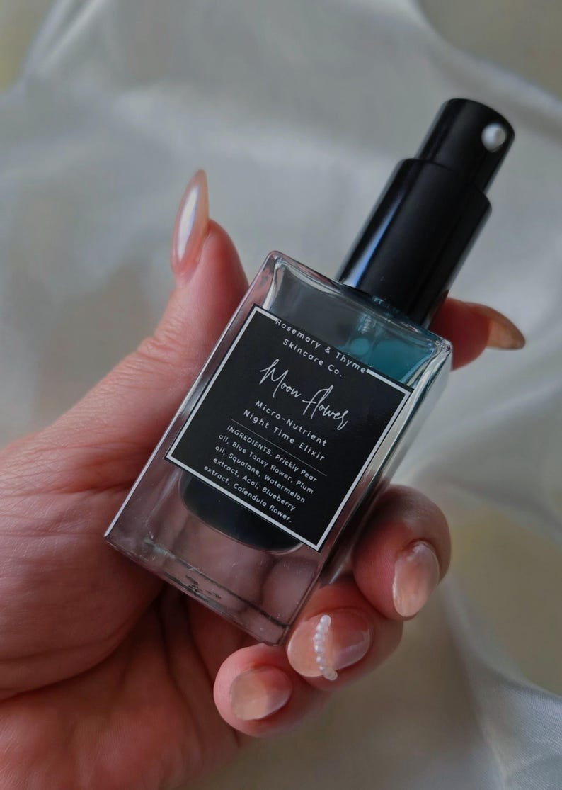 May include: A rectangular glass bottle of Rosemary & Thyme Skincare Co. Moon Flower Micro-Nutrient Night Time Elixir with a black pump dispenser. The label lists ingredients including Prickly Pear oil, Blue Tansy flower, Plum oil, Squalane, Watermelon oil, Acai, Blueberry extract, and Calendula flower.