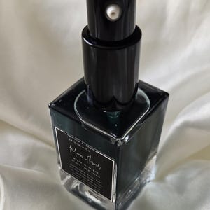May include: A square glass bottle containing a dark liquid, topped with a black pump dispenser. The label reads Rosemary & Thyme Skincare Co. Moon Flower Micro-Nutrient Night Elixir, with a list of ingredients printed in white text on a black background.