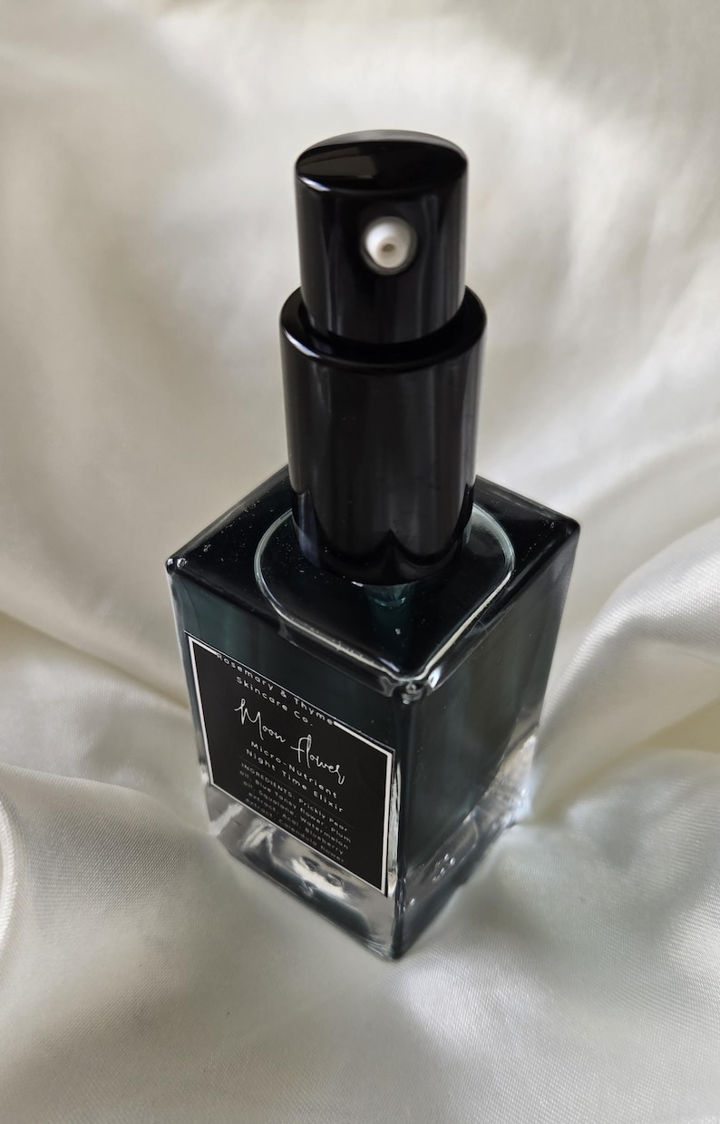 May include: A square glass bottle containing a dark liquid, topped with a black pump dispenser. The label reads Rosemary & Thyme Skincare Co. Moon Flower Micro-Nutrient Night Elixir, with a list of ingredients printed in white text on a black background.