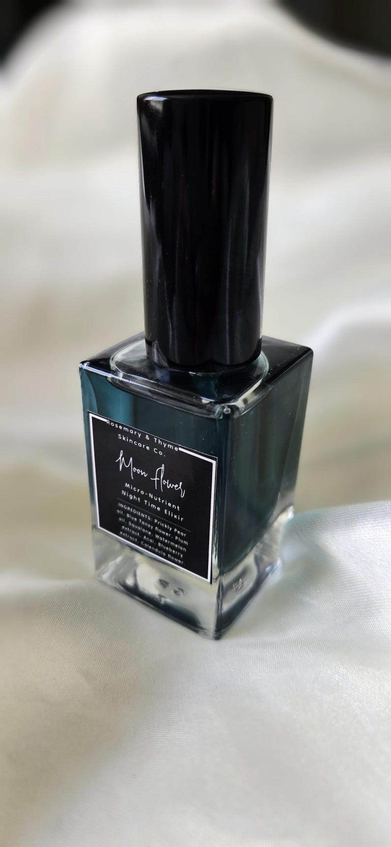 May include: A square glass bottle containing a dark teal liquid with a black cap. The label reads Rosemary & Thyme Skincare Co. Moon Flower Micro-Nutrient Night Time Elixir, listing ingredients including Prickly Pear oil, Blue Tansy flower, and Plum oil.