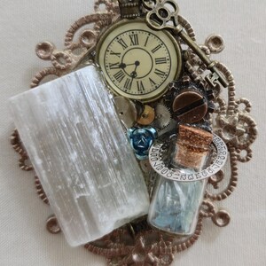May include: A steampunk-style assemblage featuring a vintage pocket watch, key, and gears. A large, rectangular, translucent crystal and a small glass bottle with blue contents are also included. The arrangement is set on a decorative, bronze-colored filigree.