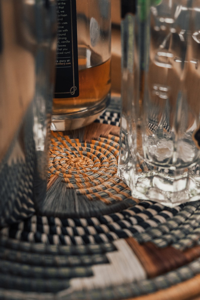 May include: A clear glass bottle with a brown liquid inside, sitting on a woven coaster with a black and white pattern. The bottle has a black label with white text that reads "at the that d, we artisan and um uses bose use with round strong in, vanilla leaves that you piced rum! le story at: distillery.com".