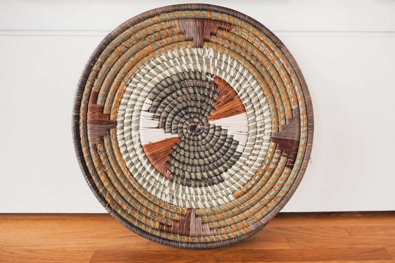 May include: A round woven wall hanging with a circular pattern in shades of brown, green, and white.
