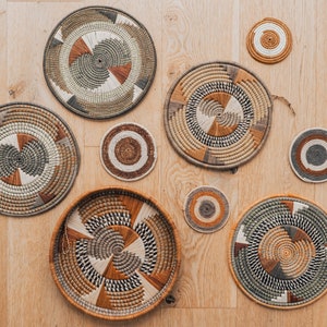 May include: A set of seven woven wall decor pieces in various sizes and patterns. The pieces are made of natural materials and feature a variety of colors, including brown, beige, and green.
