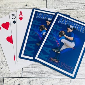 Può includere: Carte da gioco a tema baseball. Le carte includono un 7 di cuori, un 5 di picche e un As di cuori. Due carte hanno uno sfondo blu con un'immagine di un giocatore di baseball e i nomi "Sapphire" e "Kayser" stampati.