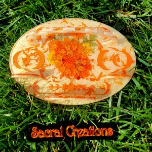 May include: Orange and yellow resin tray with a sun and moon design. The tray has a raised edge and is perfect for holding small items. The tray is on a bed of green grass. The text "Sacral Creations" is visible in the lower right corner of the image.