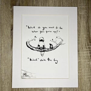 Puede incluir: Una impresión artística enmarcada con una ilustración en blanco y negro. La obra representa a un niño sentado en una rama, con la cita "¿Qué quieres ser cuando seas mayor?" y "Amable" dijo el niño.