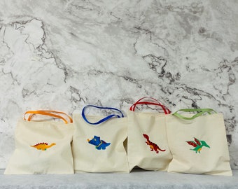 May include: Four white canvas tote bags with colorful dinosaur designs. The bags have different colored handles: orange, blue, red, and green.