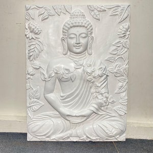 May include: White ceramic wall sculpture of a meditating Buddha surrounded by floral designs.