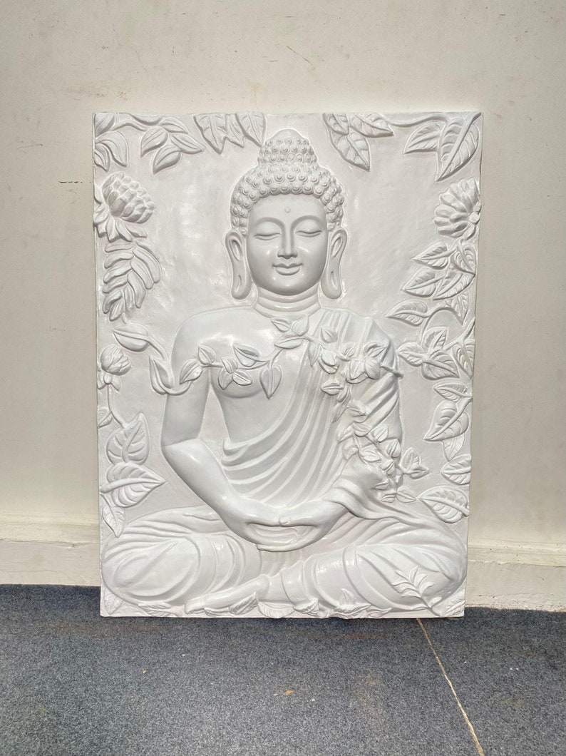 May include: White ceramic wall sculpture of a meditating Buddha surrounded by floral designs.