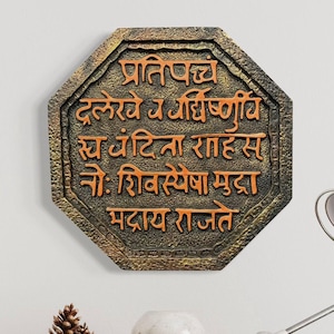 May include: Octagonal wall decor with a gold and brown finish. The decor features an inscription in the Marathi language: "प्रतिपच्च दलेरे व गिरीध्वणी स्य जहिता राहास नो: शिवसेवा मुदा मदाय राजते".