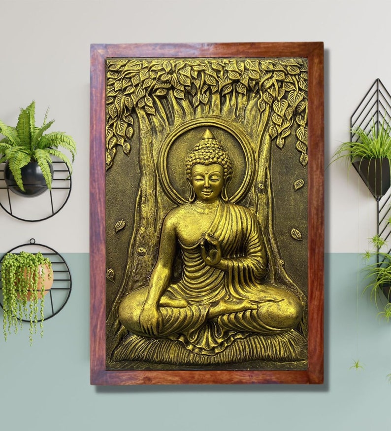 May include: A gold-colored Buddha statue in a seated meditation pose, surrounded by leaves and a tree trunk, framed in a dark wood frame.