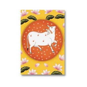 Puede incluir: Una vaca blanca con manchas naranjas se representa en un c&iacute;rculo sobre un fondo amarillo con flores de loto rosas. La vaca est&aacute; mirando hacia la derecha y tiene una cuerda marr&oacute;n alrededor del cuello.