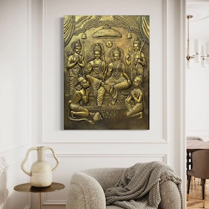 May include: A gold-toned metal wall sculpture depicting a group of Hindu deities. The sculpture is detailed with intricate carvings and features a central figure with a crown and a bow and arrow. The sculpture is set against a dark background.