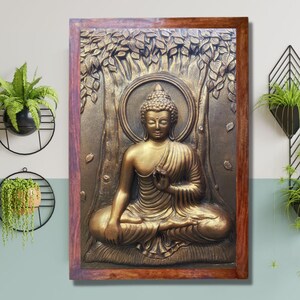 May include: A gold-colored Buddha statue in a wooden frame. The statue is sitting in a meditative pose with hands in the lap. The statue is surrounded by a tree with leaves.