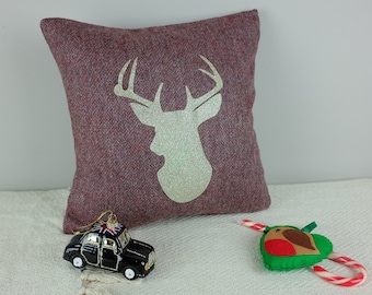 Peut inclure: Un coussin en tweed rouge et brun avec une silhouette de cerf en paillettes dorées. Le coussin est sur une surface blanche avec un ornement de voiture noire et un ornement d'oiseau en feutre vert.