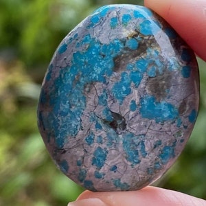 May include: A smooth, oval-shaped turquoise stone with a mottled pattern of blue and grey. The stone has a natural, polished finish.