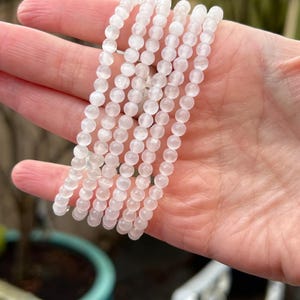 May include: A stack of white gemstone bracelets with round beads. The bracelets are made of white moonstone beads.