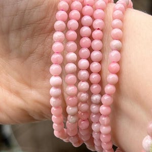 May include: A stack of pink opal beaded bracelets. The bracelets are made of small, round beads and are stacked on top of each other.