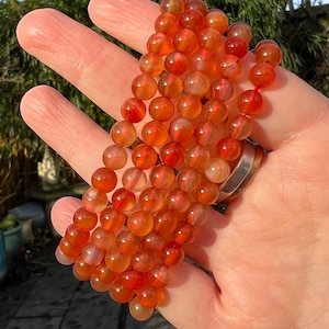 Puede incluir: Una hebra de cuentas de cornalina, una piedra semipreciosa, en tonos naranja y rojo. Las cuentas son redondas y lisas, y están enhebradas en un cordón fino.