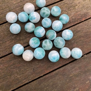 May include: A collection of 20 blue and green gemstone spheres, also known as blue apatite, on a wooden surface. The spheres are smooth and polished, with a variety of patterns and textures.