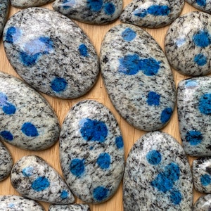 May include: A collection of polished blue and white speckled stones, also known as kyanite, with a variety of shapes and sizes.
