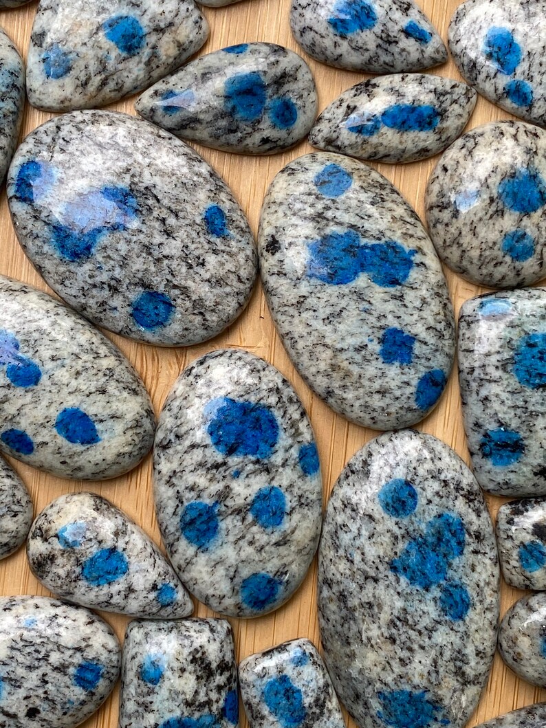 May include: A collection of polished blue and white speckled stones, also known as kyanite, with a variety of shapes and sizes.