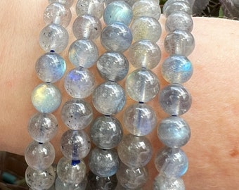 May include: A stack of five bracelets made of iridescent grey labradorite beads. The beads are round and smooth, and the bracelets are strung on elastic.