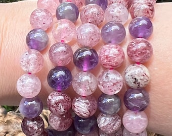 May include: A set of six bracelets made with amethyst and rose quartz beads. The beads are a mix of purple and pink with white and brown inclusions. The bracelets are stacked on a person's wrist.