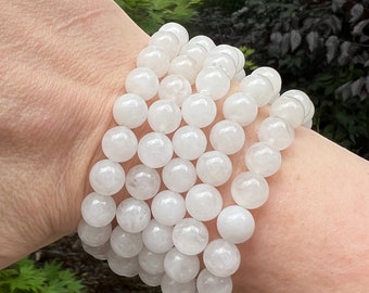 May include: A white gemstone bracelet with round beads. The bracelet is made of multiple strands of beads and is worn on a person's wrist.