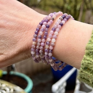 May include: A stack of purple and pink gemstone bracelets. The bracelets are made of small, round beads and are layered on a person's wrist.