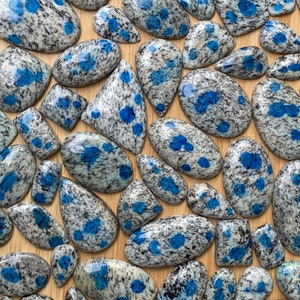 May include: A collection of blue and gray speckled gemstone cabochons. The stones are various shapes and sizes, and have a unique speckled pattern.